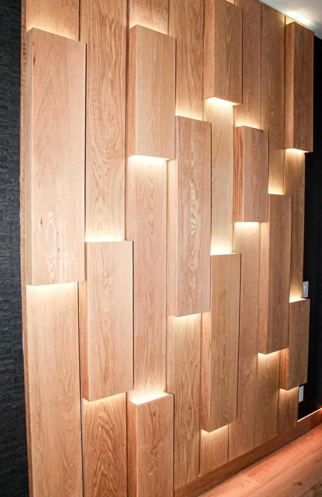 Angled view of a backlit staggered wood plank wall against a dark textured surround