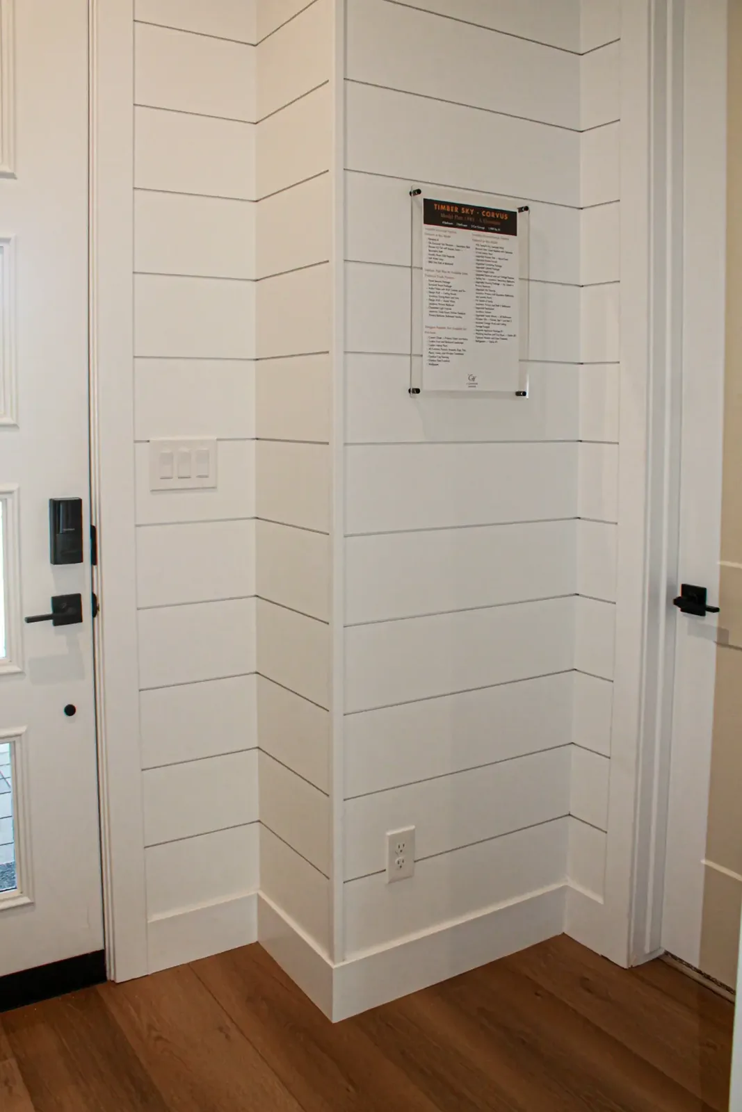 White shiplap wrapping an interior corner beside a front door, with painted baseboard and a switch plate