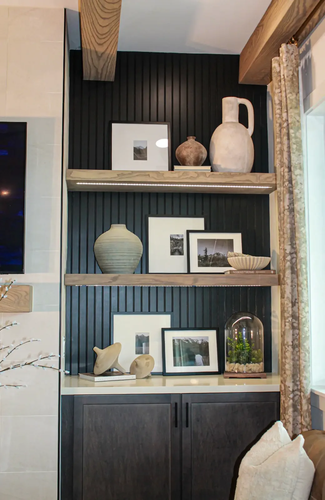 Two lit wood floating shelves against a black beadboard back panel above a pair of dark cabinet doors
