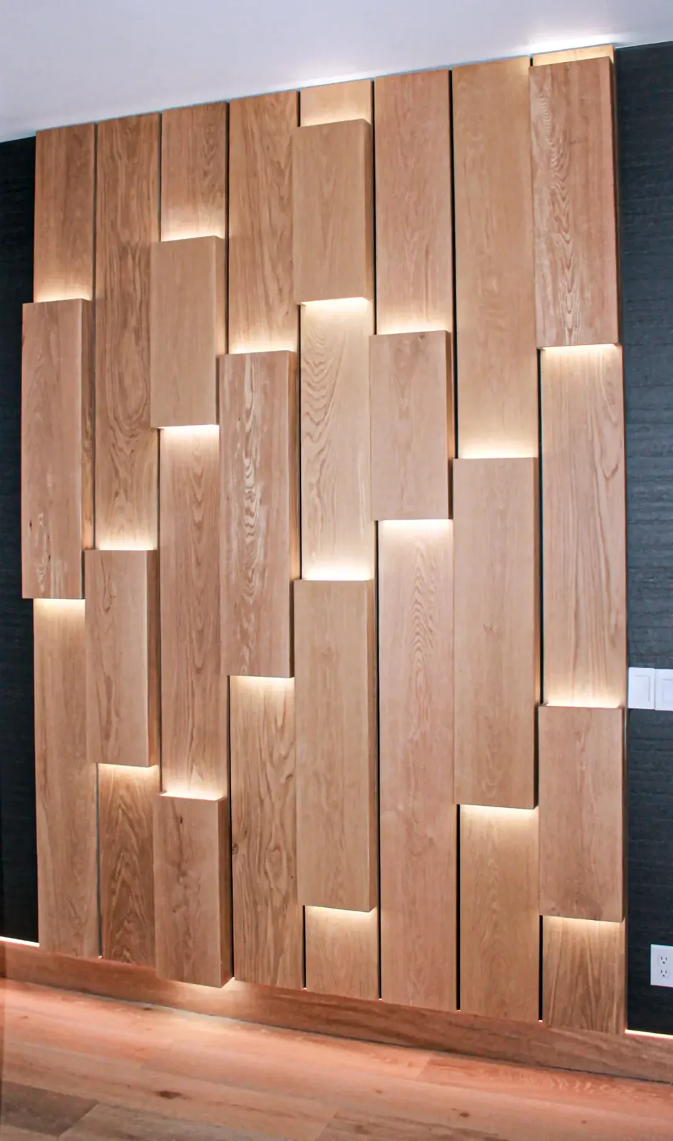 Feature wall of staggered wood planks with concealed lighting washing down each stepped edge