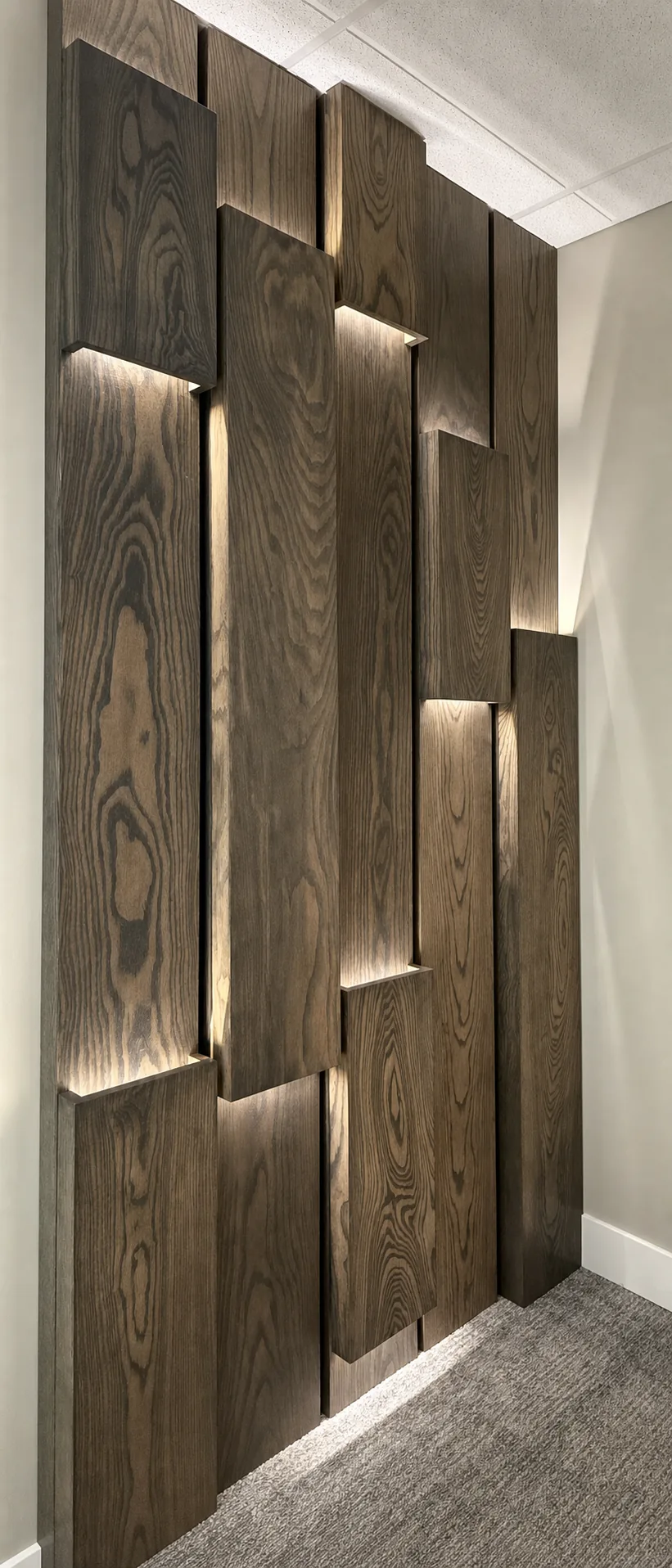 Interior accent wall of staggered vertical wood panels with recessed lighting between panels