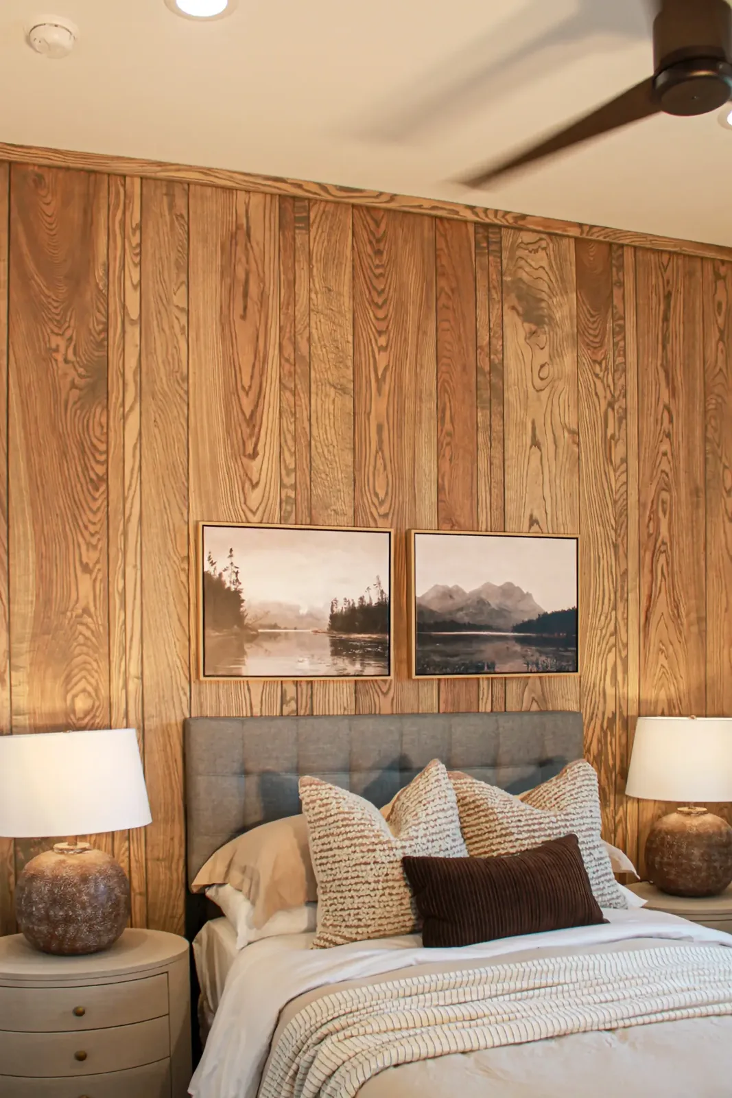 Bedroom wall clad floor to ceiling in vertical wood planks behind an upholstered headboard and two framed prints
