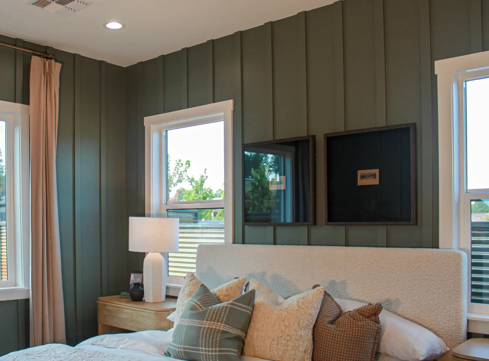 Green board and batten wall behind an upholstered bed, with a framed wall-mounted TV and framed art