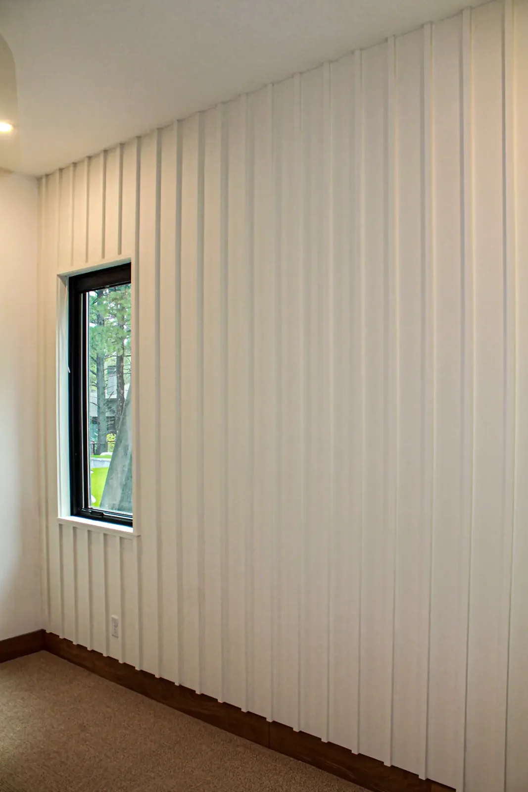 Painted vertical board and batten wall wrapping around a small black-framed window