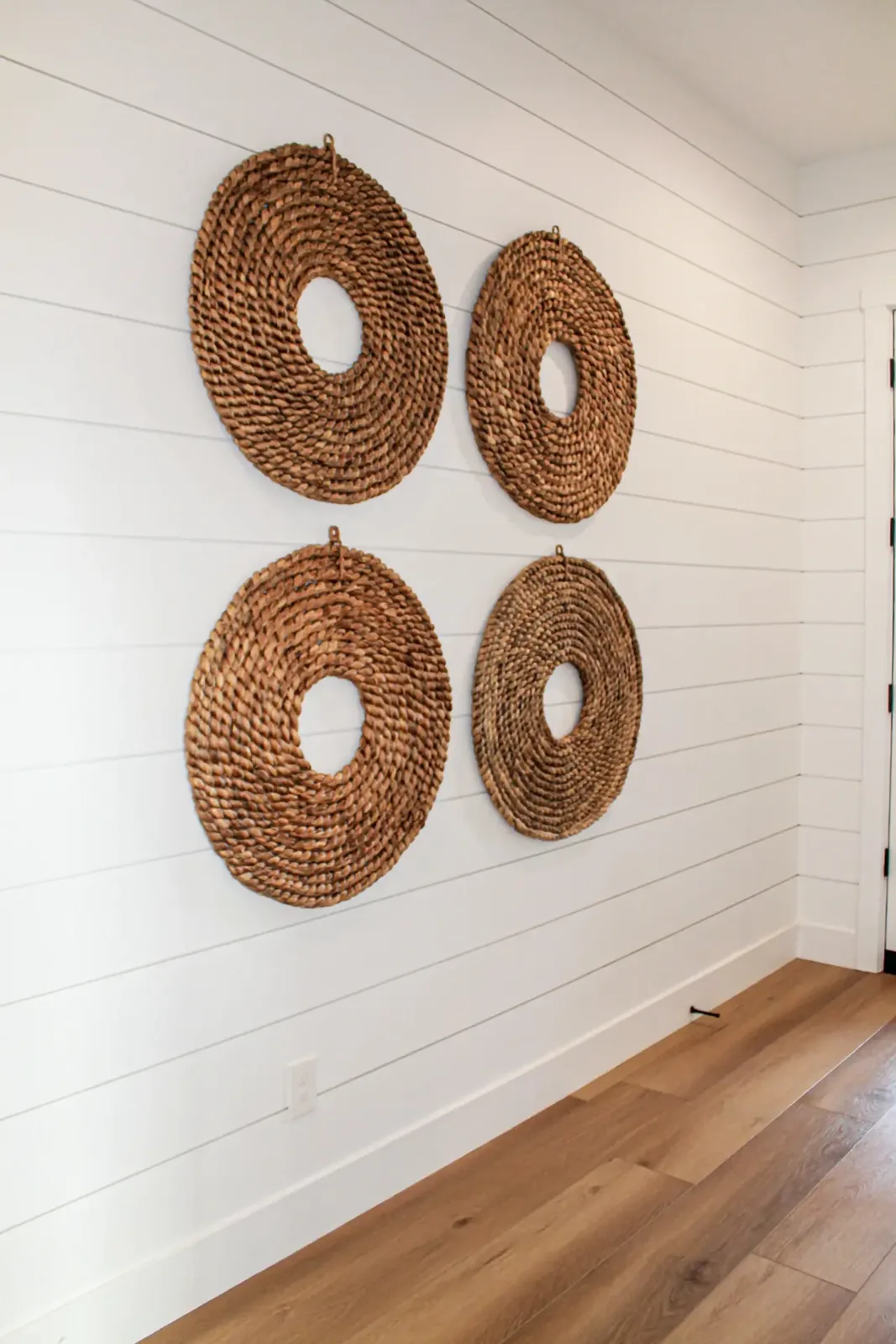 White horizontal shiplap wall holding four round woven wall pieces, with painted baseboard below